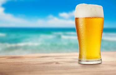 glass of beer on wooden table on background of sea