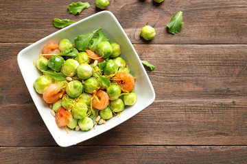 Bowl of delicious salad with Brussels sprouts and shrimps on wooden table, top view. Space for text
