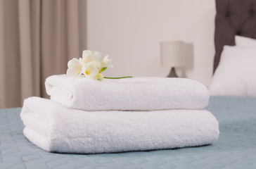 Fototapeta na wymiar Stack of fresh towels with flowers on bed in hotel room