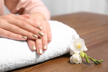 Obraz na płótnie Canvas Woman with gold manicure on rolled towel at table, closeup. Nail polish trends