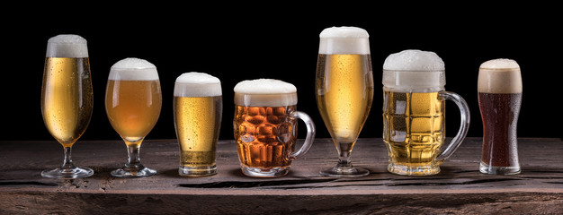 Beer assortment. Cold different glasses of beer on the wooden table at the black background. - obrazy, fototapety, plakaty