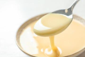 Spoon of pouring condensed milk over bowl on table, closeup with space for text. Dairy products