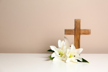 Composition with wooden cross and blossom lilies on table against color background, space for text