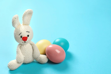 Cute Easter bunny toy and dyed eggs on color background, space for text