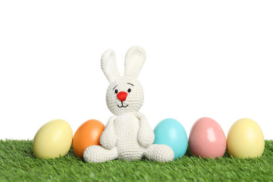 Cute Easter bunny toy and dyed eggs on green grass against white background