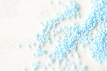 Seed beads light blue color scattered on a textile background close up
