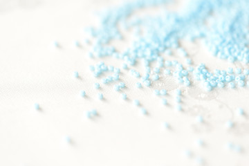 Seed beads light blue color scattered on a textile background close up
