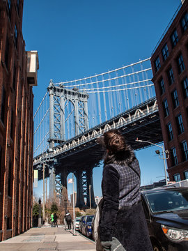 Young woman taking picture at Manhattan bridge from road on sunny winter day. New York, USA