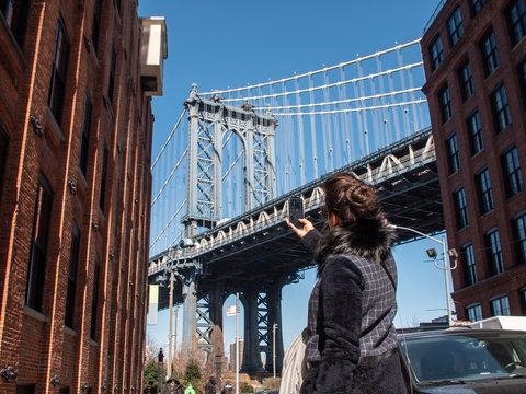 Young woman taking picture at Manhattan bridge from road on sunny winter day. New York, USA