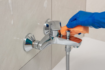 Close-up of the shower faucet and shower head cleaning process from lime scale, white chalk sediment and stains using a commercial soap scum remover. Bathroom cleaning and disinfection, cleanup