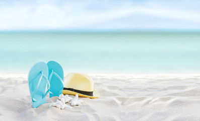 Beach summer holiday banner background. Flip flops and hat on sand near ocean. Summertime accessories on seaside. Tropical vacation and relax travel concept. Top view and copy space. Selective focus