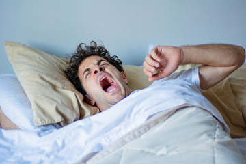 Young man yawning in bed.