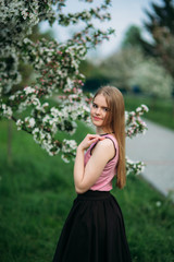 Beautiful blond hair girl standing in front of the blooming tree. Charming lady in dress