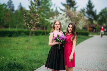 Obraz na płótnie Canvas Two sisters walking outside in spring park. They hold a bouqet of lilac and smile