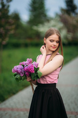 Attractive blond hair girl hold a bouquet of lilac in hands. Charming girl outside
