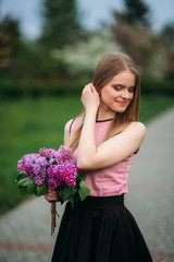 Attractive blond hair girl hold a bouquet of lilac in hands. Charming girl outside