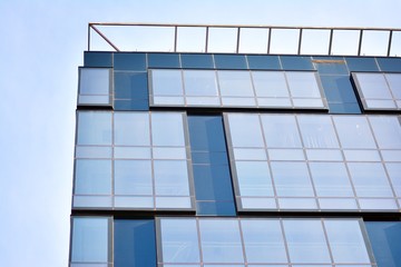 Fototapeta premium New office building in business center. Wall made of steel and glass with blue sky. 
