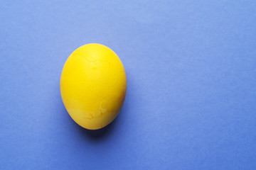 Stained in yellow Easter egg as an attribute of Easter celebration on blue background.