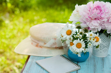 Summer flowers, daisies and peonies and straw hat on a wooden table in the summer garden.