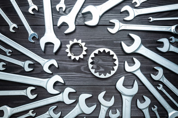 Conceptual background. A set of new chrome wrenches and gear on dark wooden workbench.