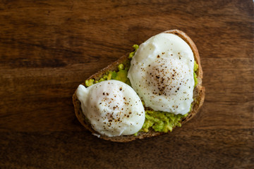 Avocado toast with poached eggs. Served on dark wooden surface
