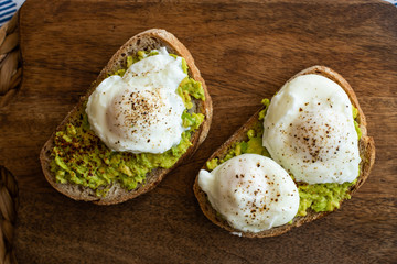 Avocado toast with poached eggs. Served on dark wooden surface