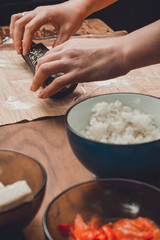 A female cook prepares sushi in the kitchen and wraps a letter to the nori in the roll