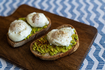 Avocado toast with poached eggs. Served on dark wooden surface