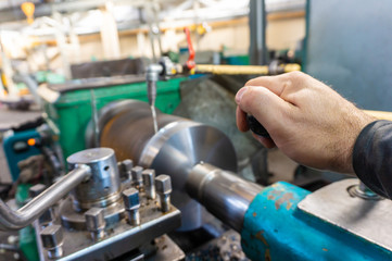 The hand of the machine operator creates a mechanical switch on the lathe.