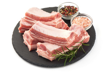 Raw pork meat ribs with rosemary on a slate shale plate, close-up, isolated on white background