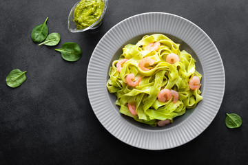 Boiled fettuccine pasta with fresh spinach pesto and shrimps on black background. Italian cuisine. Healthy dish for lunch. Top view