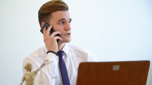 Manager young man accepts applications on the phone sitting at the computer. Office worker is talking on a mobile phone. Office work concept.