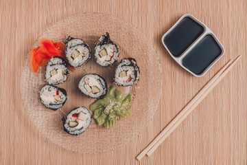 Sushi rolls on a round plate with sticks and soy sauce, top view