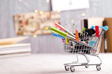 Creative image with stationery in shopping cart and notebooks, gift cards and fairy lights...