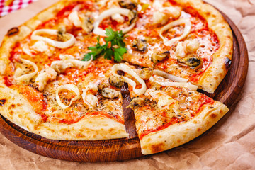 Italian Pizza with seafood and mozzarella cheese on wooden cutting board. Close up