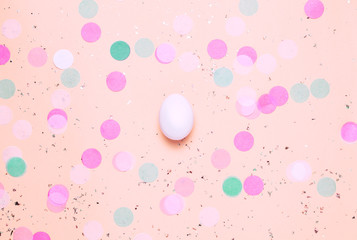 Three eggs in paper pink nest on pink table with confetti. Top view, flat lay