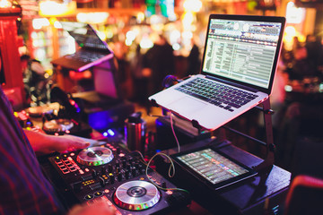Hands of DJ mix tracks on digital turntable and software on laptop with professional mixing...