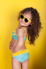 Little girl in a bathing suit and sunglasses on a yellow background