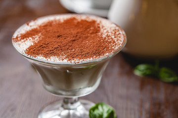 Italian dessert Tiramisu in portion glass on wooden table. Close up