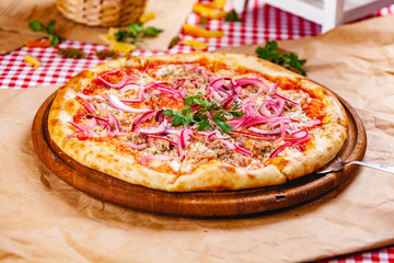 Pizza with tuna and red onion on wooden cutting board. Close up