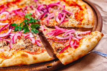 Pizza with tuna and red onion on wooden cutting board. Close up