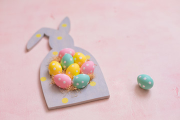 Colorful polka dot easter eggs in rabbit-shaped frame on pink concrete background