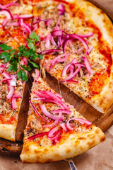 Pizza with tuna and red onion on wooden cutting board. Close up