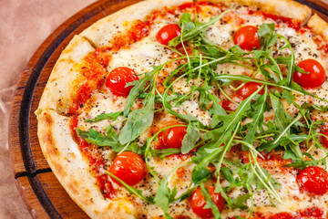 Italian Pizza with tomatoes, mozzarella cheese and arugula on wooden cutting board. Close up