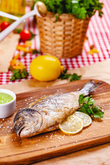 Grilled dorado fish with lemon and sauce on wooden board. Close up