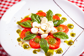 Traditional Italian caprese salad with sliced tomatoes, mozzarella cheese, basil and pesto sauce on white plate. Close up