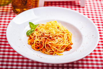 Italian cuisine. Spaghetti bolognese with meat, parmesan cheese and tomatoes on white plate. Close up