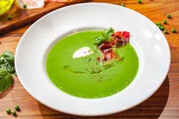 Green pea cream soup with bacon in white plate. Close up