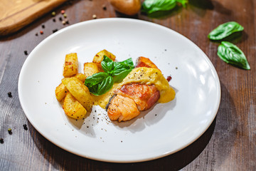 Grilled salmon fillet wrapped in bacon and potato wedges on white plate. Close up