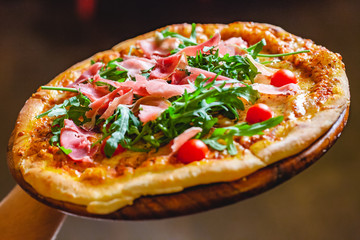Chef holding Italian Pizza with prosciutto (parma ham), arugula (salad rocket) and cherry tomatoes. Close up